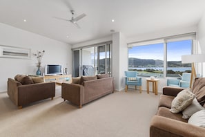 A modern living room with a sofa, armchairs, a TV, and a view of a lake.