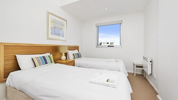 A hotel room with two beds, a window, a framed picture, and a small table.