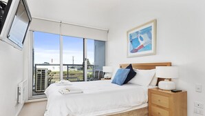 A bedroom with a bed, bedside table, lamp, and a painting on the wall.