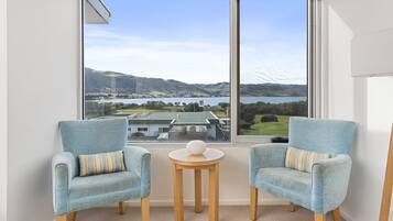A room with two armchairs, a small round table, and a large window offering a view of a landscape with hills and a body of water.