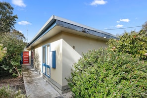 A small building with a single door and a window, surrounded by greenery.