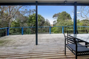 A covered outdoor deck with a table and chairs, surrounded by a blue railing and trees. - Beach Fig (Skenes Creek, Apollo Bay)