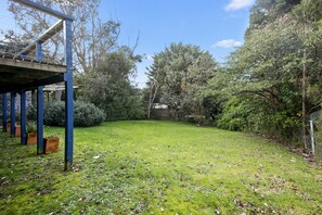 A grassy backyard with a wooden deck and a metal fence. - Beach Fig (Skenes Creek, Apollo Bay)