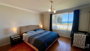Ein Schlafzimmer mit einem großen Bett, zwei Nachttischen mit Lampen, einem Fenster mit Blick ins Freie und einer Deckenleuchte.
