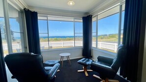 Ein Zimmer mit zwei schwarzen Ledersesseln, einem kleinen runden Tisch und großen Fenstern mit Blick auf den Ozean und einen weißen Zaun.