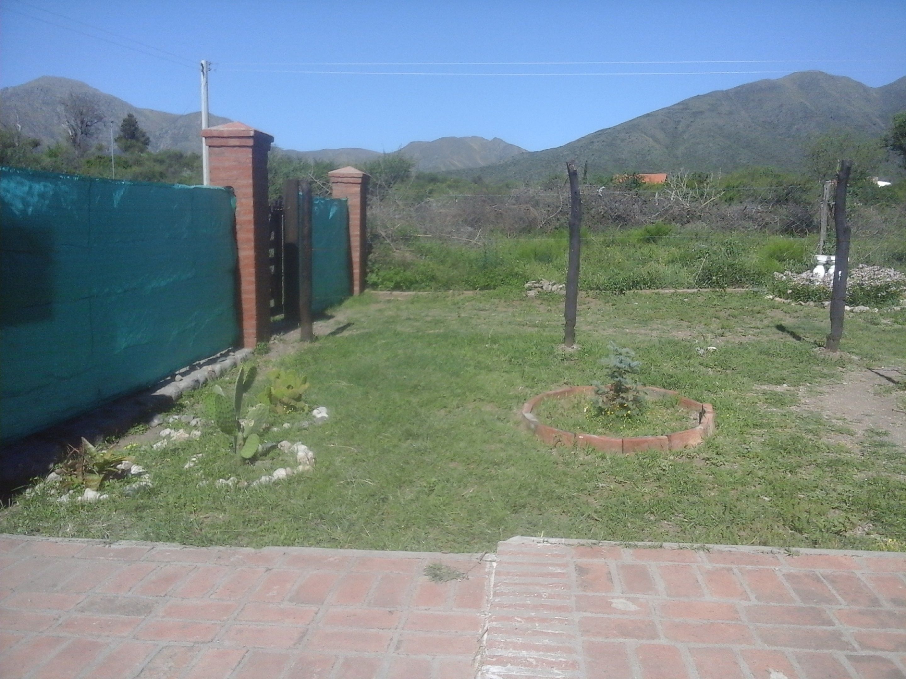 A fenced backyard with a grassy area, a brick pathway, and a small circular garden bed.