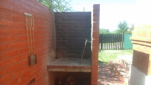 An outdoor brick oven with a chimney, surrounded by a brick wall and a wooden fence. - Cabañas San Gabriel Arcangel (Capilla del Monte)