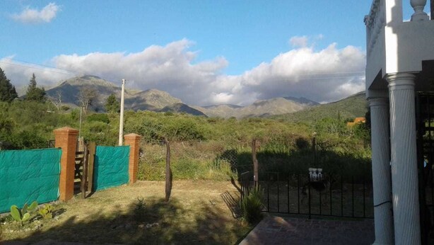 A property with a fenced yard, a gate, and a view of mountains in the background. - Cabañas San Gabriel Arcangel (Capilla del Monte)