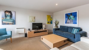 A modern living room with a flat-screen TV, a wooden coffee table, a blue sofa, and artwork on the walls. - Carrageen (Lorne)