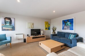 A modern living room with a flat-screen TV, a wooden coffee table, a blue sofa, and artwork on the walls. - Carrageen (Lorne)