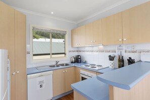 A modern kitchen with wooden cabinets, a built-in dishwasher, a stove, and a window with a view of greenery.