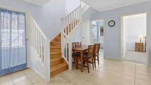 A staircase leading to a dining area with a table and chairs, a clock on the wall, and a door leading to another room. - Beach Retreat (Apollo Bay)