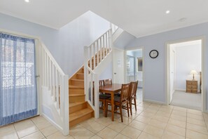 A staircase leading to a dining area with a table and chairs, a clock on the wall, and a door leading to another room.