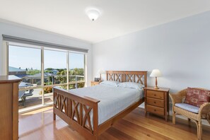 A bedroom with a large window, a wooden bed, a nightstand, a chair, and a ceiling light.
