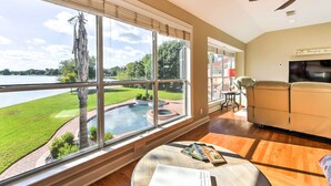 Amplia habitación con grandes ventanales que dan a un jardín cuidado y una piscina.