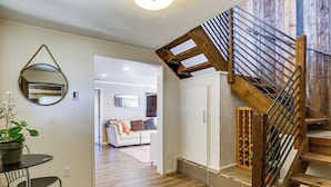 Un interior moderno con una escalera, un espejo redondo, una zona de comedor con mesa y sillas, y una sala de estar con sofá y chimenea.