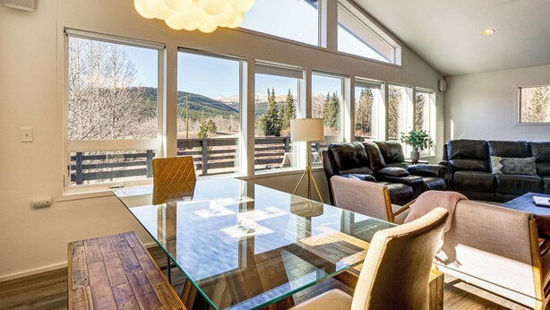 Amplia sala de estar con mesa de vidrio, sofás de cuero y ventanas grandes con vistas a la montaña.