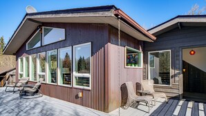 Una terraza de madera con mobiliario exterior y grandes ventanales.