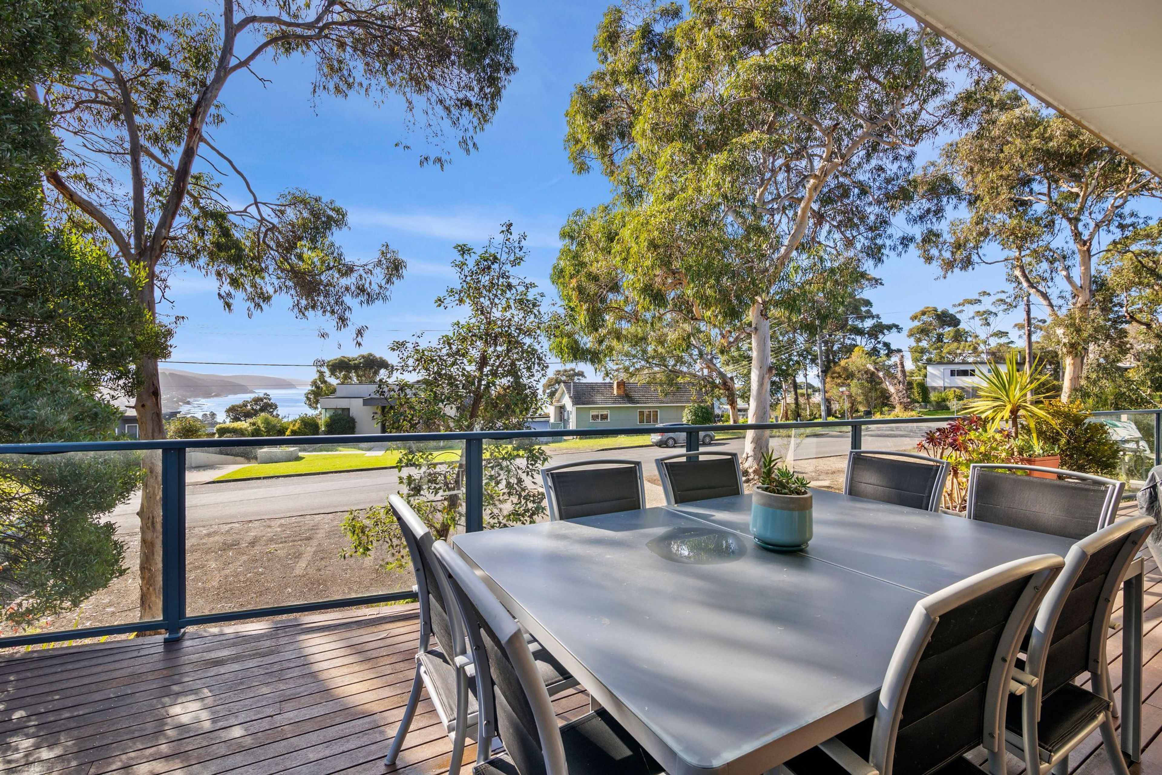 A balcony with a table and chairs, overlooking a street and greenery.
