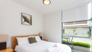 A modern hotel room with a large bed, a nightstand, a lamp, and a view of the outside. - Anglesea River Apartment 23 (Anglesea)