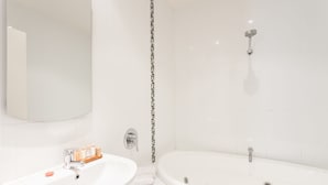 A modern bathroom with a large bathtub, a separate shower area, and a sink with toiletries. - Anglesea River Apartment 23 (Anglesea)