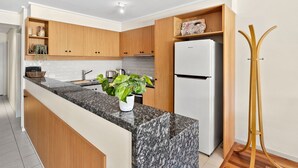 A modern kitchen with wooden cabinets, a granite countertop, a white refrigerator, and a plant on the island. - Apartment 23 Pacific Apartments (Lorne)