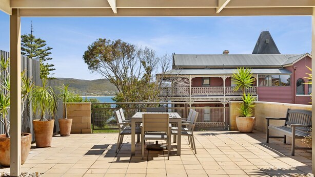 An outdoor patio with a table and chairs, surrounded by potted plants and overlooking a scenic view. - Apartment 23 Pacific Apartments (Lorne)