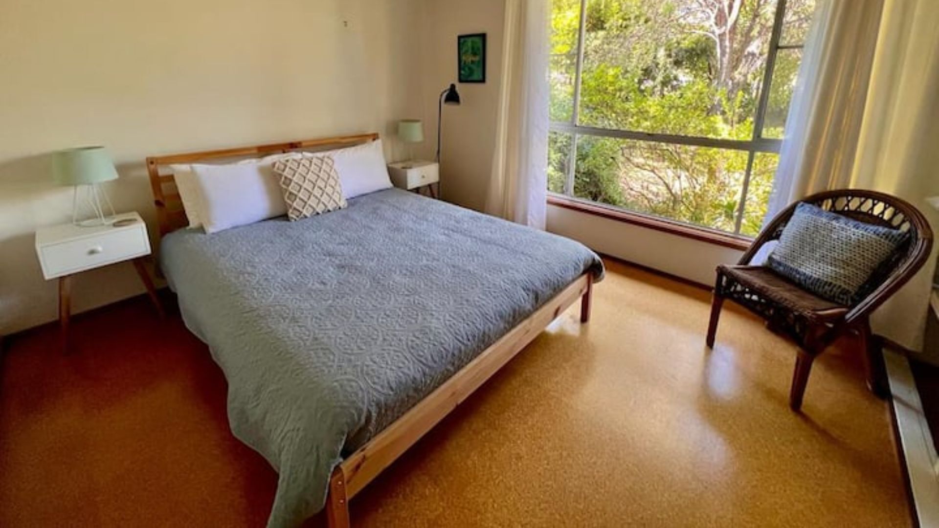 A bedroom with a bed, a chair, a nightstand, and a window with a view of trees.