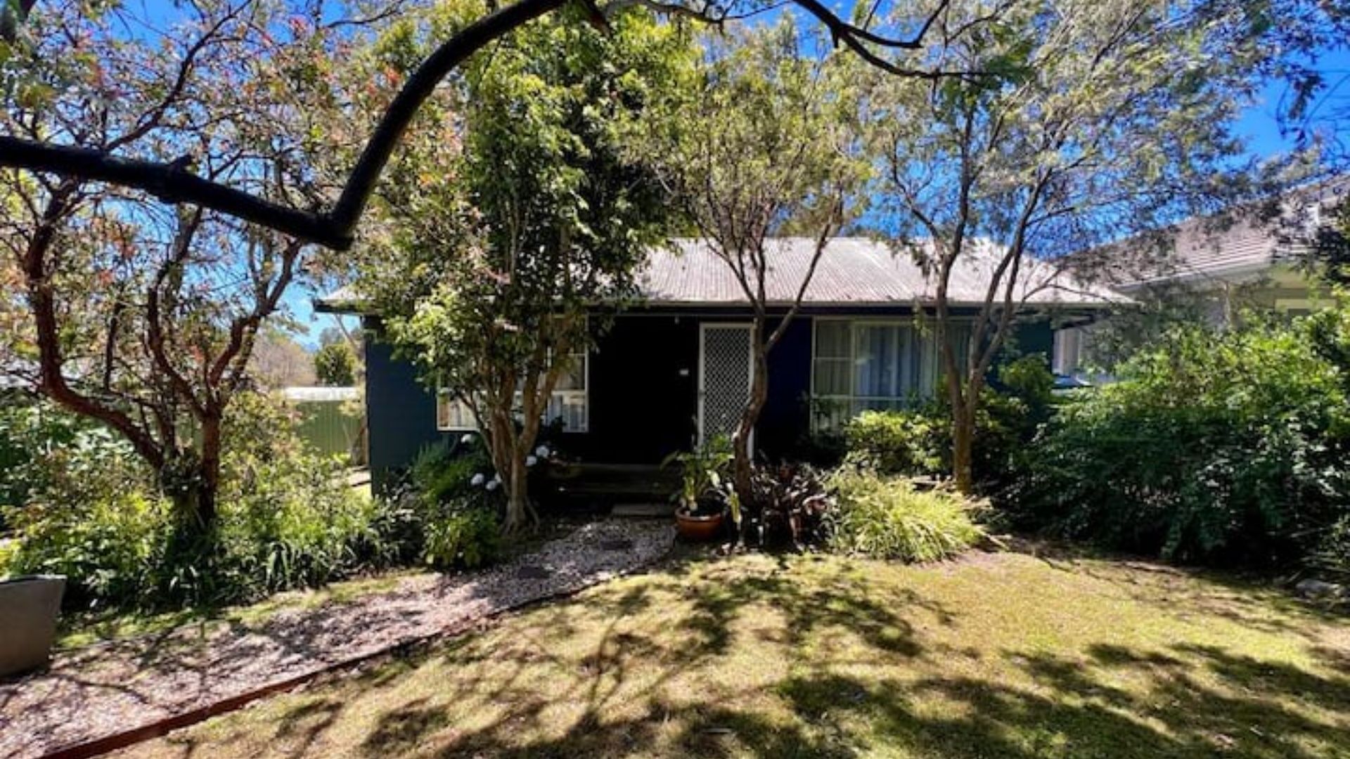 A house with a front yard, a pathway leading to the entrance, and a variety of plants and trees.