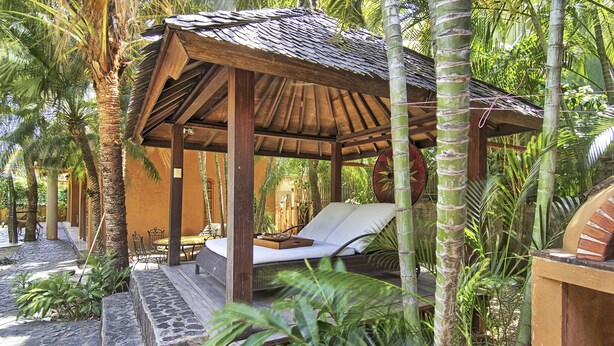 A wooden gazebo with a cushioned bench and a table, surrounded by tropical plants and palm trees. - Villa Doña Iñes - Privacy! Gorgeous home, guest house & pool, free wifi! (Tamarindo)