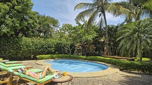 A poolside area with lounge chairs and a small table, surrounded by lush greenery and palm trees. - Villa Doña Iñes - Privacy! Gorgeous home, guest house & pool, free wifi! (Tamarindo)
