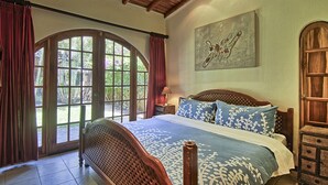 A bedroom with a large bed, wooden headboard, and a view through a glass door. - Villa Doña Iñes - Privacy! Gorgeous home, guest house & pool, free wifi! (Tamarindo)