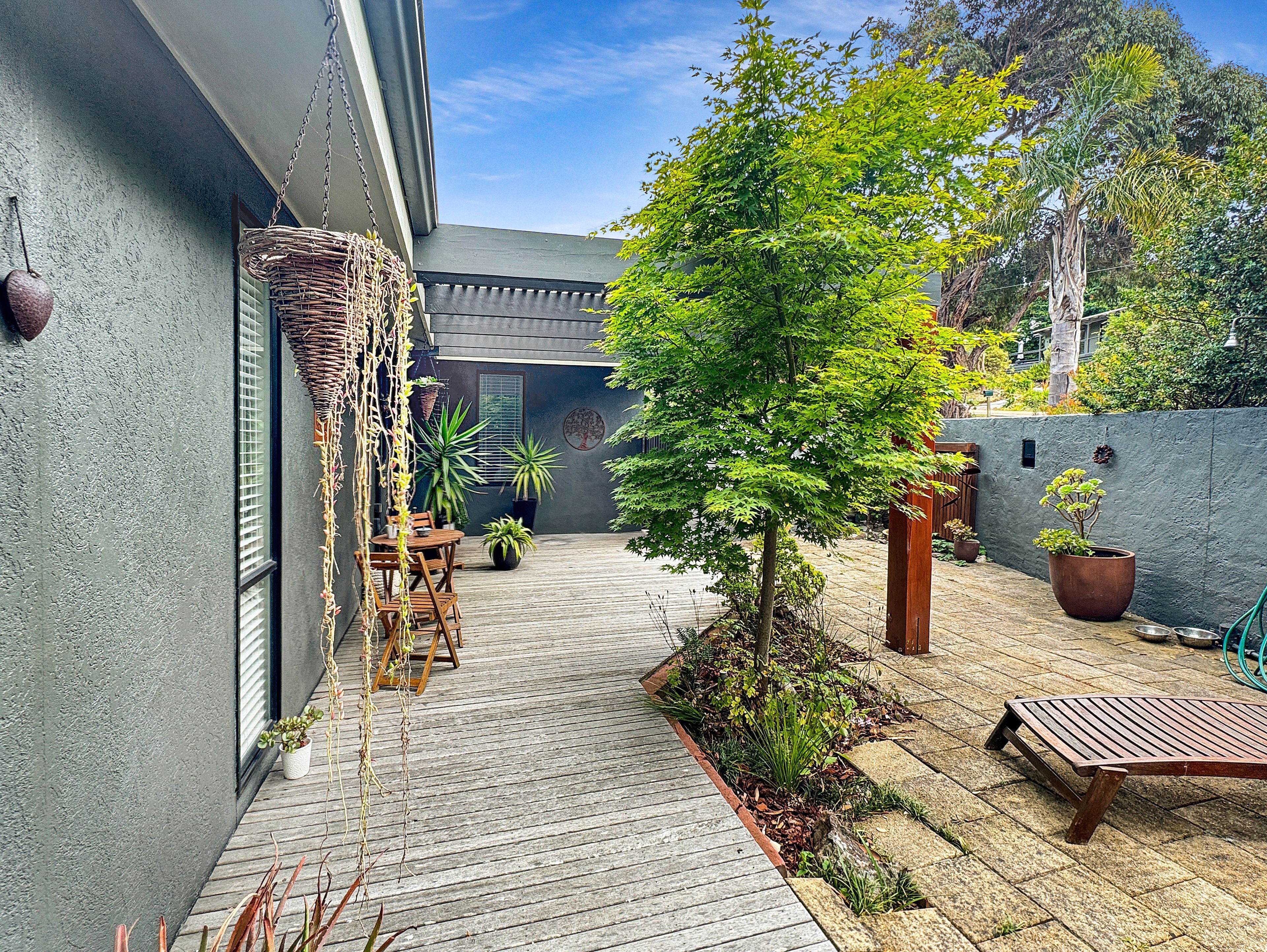 A wooden deck with a table and chairs, surrounded by potted plants and a small tree.