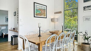 A dining area with a wooden table, white chairs, a ceiling fan, and a view of the outdoors. - SeaEsta - Modern Beachside Escape North Lorne (Lorne)
