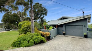A modern two-story house with a garage, surrounded by a well-maintained lawn and various shrubs. - SeaEsta - Modern Beachside Escape North Lorne (Lorne)