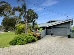 A modern two-story house with a garage, surrounded by a well-maintained lawn and various shrubs. - SeaEsta - Modern Beachside Escape North Lorne (Lorne)