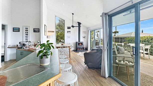 A modern kitchen with a bar area, dining space, and a cozy seating area with a fireplace. - SeaEsta - Modern Beachside Escape North Lorne (Lorne)