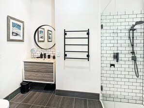 A bathroom with a white vanity, a round mirror, a towel rack, and a glass shower enclosure with a tiled wall. - SeaEsta - Modern Beachside Escape North Lorne (Lorne)