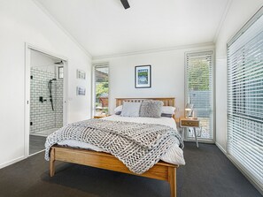 A bedroom with a large bed, a wooden headboard, a bedside table with a lamp, and a window with blinds. - SeaEsta - Modern Beachside Escape North Lorne (Lorne)
