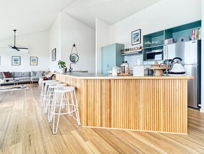 A modern kitchen with a wooden island, bar stools, a built-in oven, and a refrigerator. - SeaEsta - Modern Beachside Escape North Lorne (Lorne)
