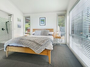 A bedroom with a wooden bed, a bedside table, a framed picture on the wall, and a window with blinds.