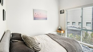 A bedroom with a bed, pillows, a bedside table, a lamp, a window with blinds, and a wall-mounted picture. - SeaEsta - Modern Beachside Escape North Lorne (Lorne)