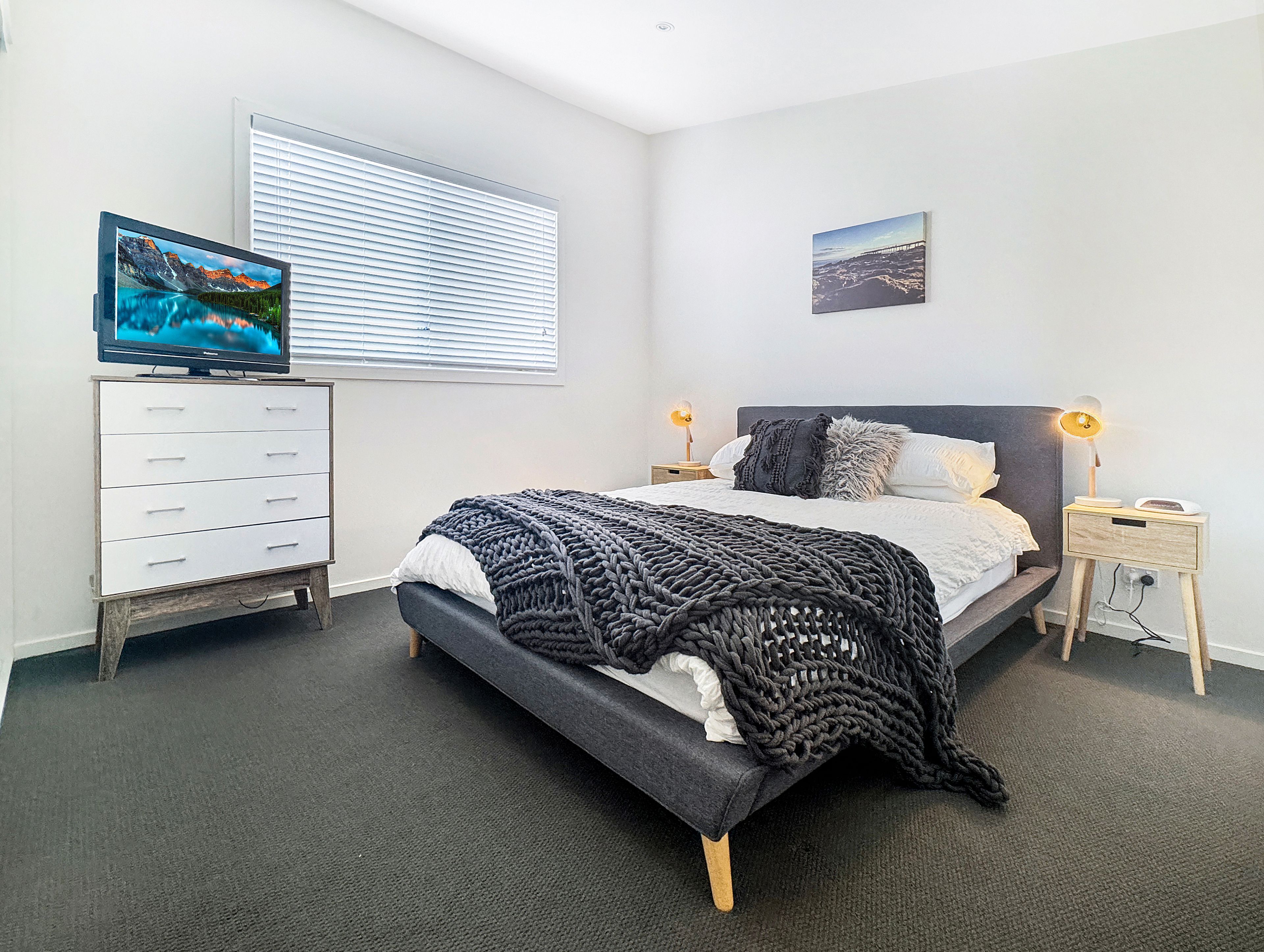 Un dormitorio con cama, cómoda, televisor y dos lámparas de noche.