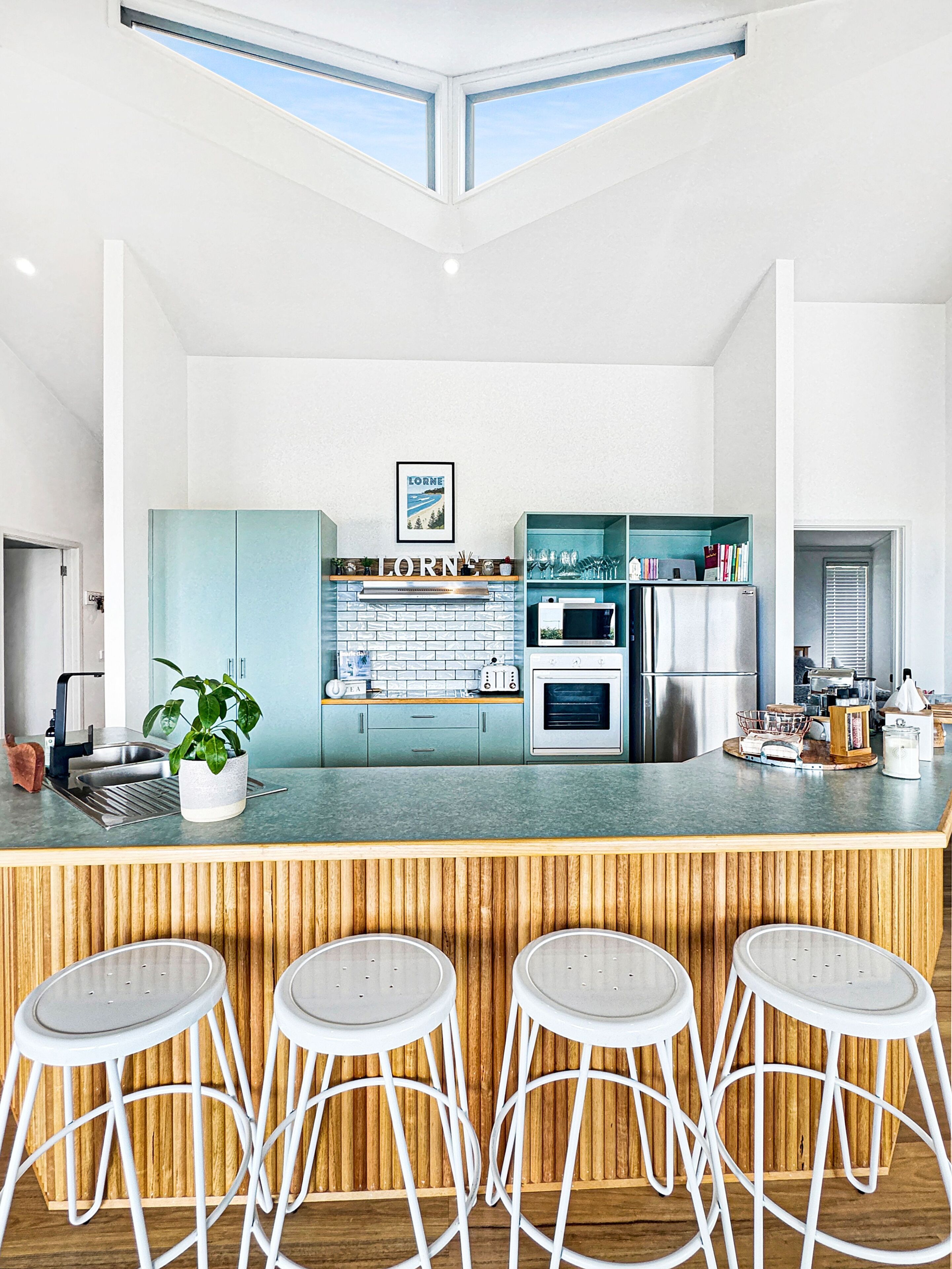 A modern kitchen with a central island, bar stools, and a view of the sky through skylights.