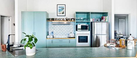 A modern kitchen with a central island, bar stools, and a view of the sky through skylights.