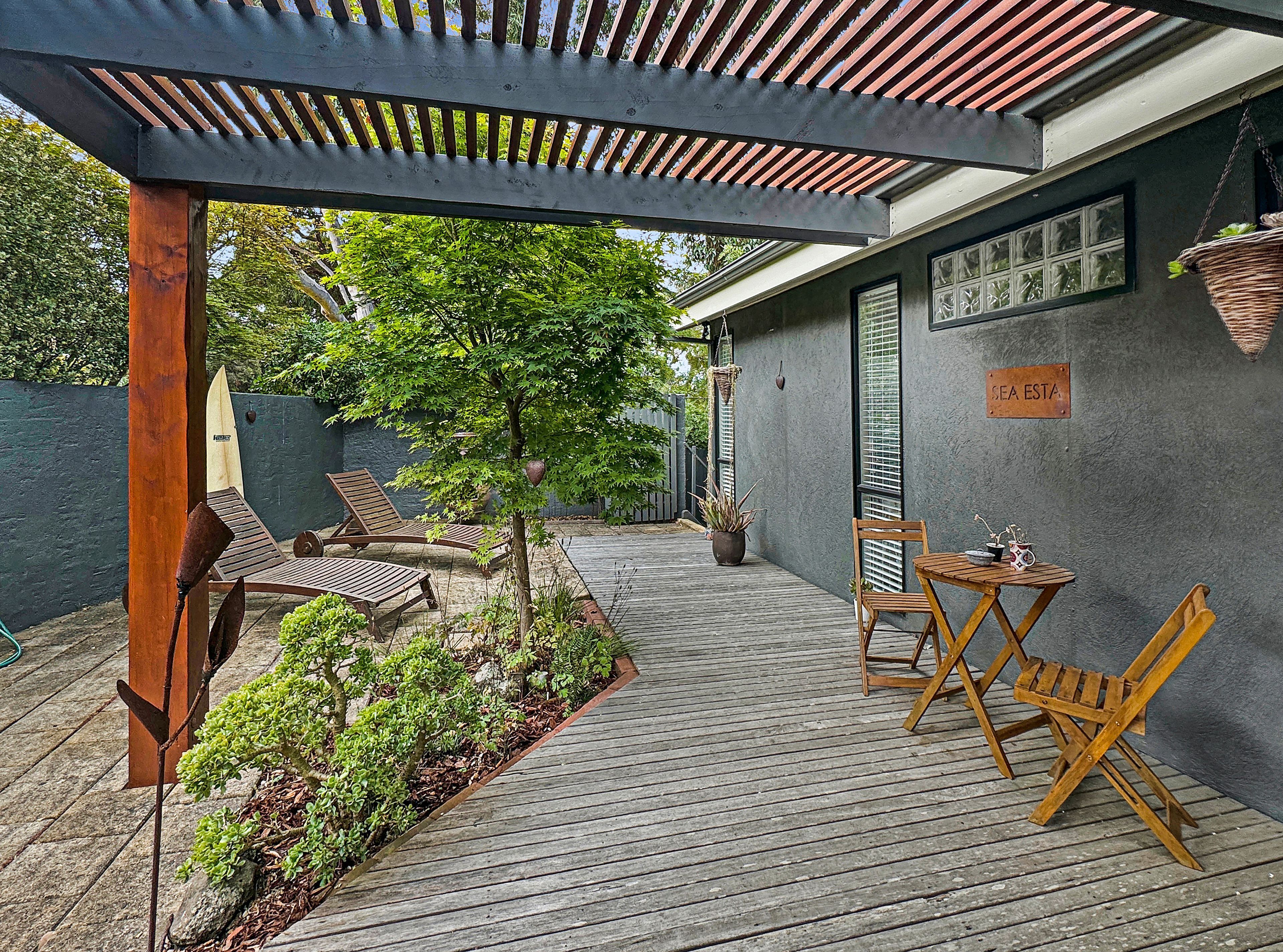 Eine Holzterrasse mit einer Pergola, Sitzgelegenheiten im Freien und einem Blumentopf.