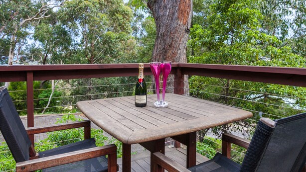 A wooden deck with a table and two chairs, a bottle of champagne, and a glass on the table.