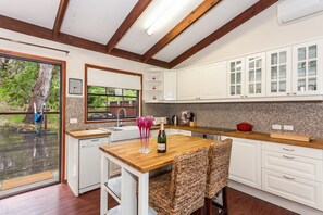 Une cuisine moderne avec des meubles blancs, une table à manger en bois et une vue sur l’extérieur.