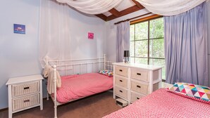 A bedroom with two beds, a bedside table, a dresser, and a window with curtains.