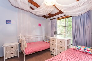 Une chambre avec deux lits, une table de chevet, une commode et une fenêtre avec des rideaux.